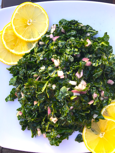 The Best Kale Salad Recipe served on a plate with lemon wedges for garnish.
