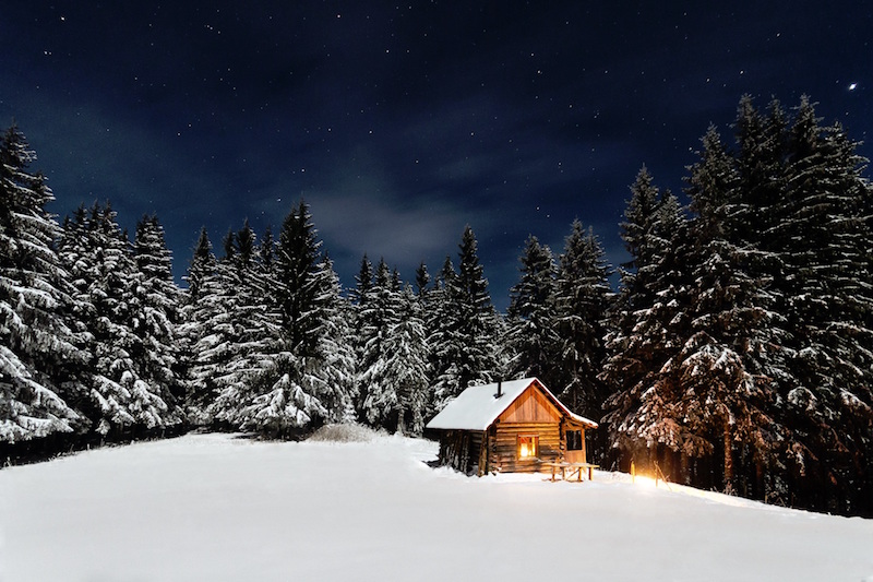 A log cabin in the snowy woods, lit up by a fire and candles is definitely hygge.